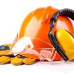 Safety gear including an orange hard hat, yellow ear protection, safety glasses, and gloves on blueprints.