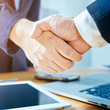 Business Agreement Handshake Close-up of a business handshake with a tablet and laptop on the desk.