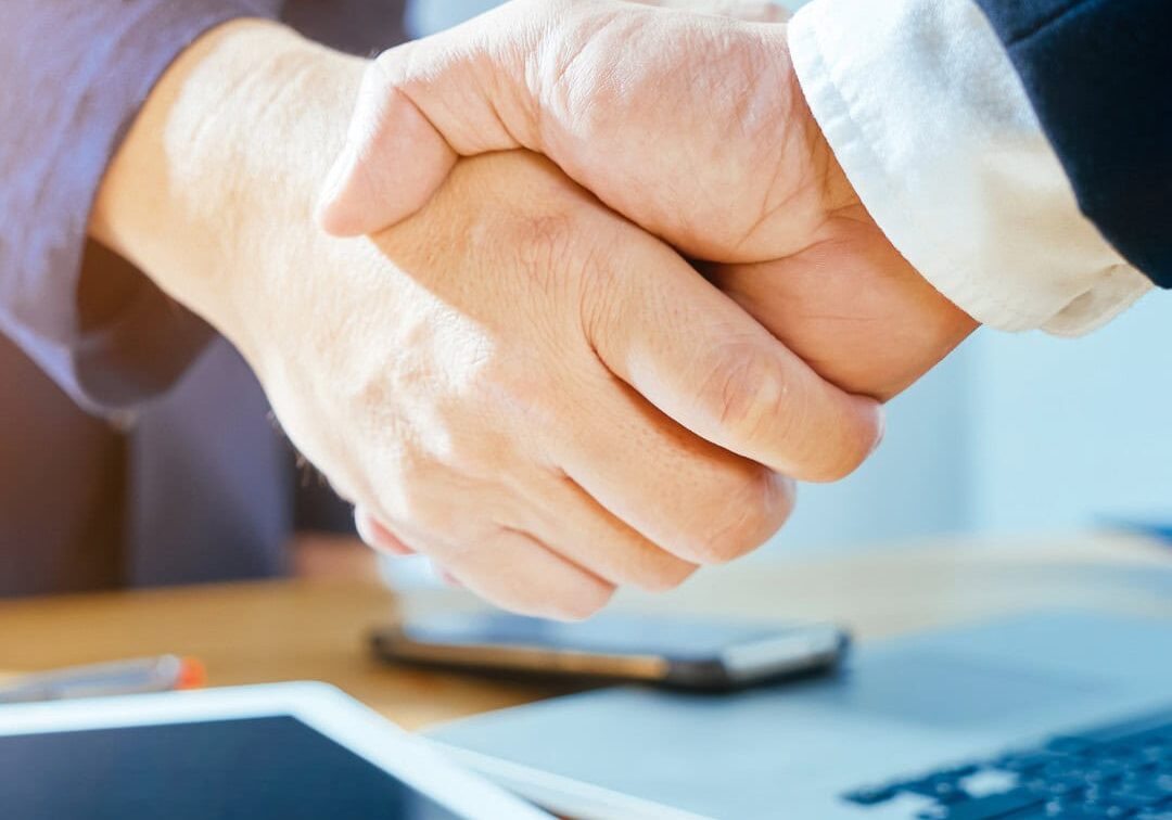 Business Agreement Handshake Close-up of a business handshake with a tablet and laptop on the desk.